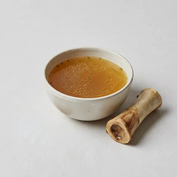 Bowl of beef bone broth with a marrow bone, an ingredient in Roots Pet soft chews for dogs